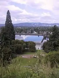 Broad view over a city from an elevated viewpoint, with a reservoir in the near distance