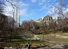 Parkland and people on pathways, with a church and high-rise buildings in the background