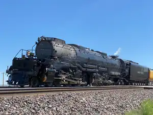 An articulated steam locomotive with a 4-8-8-4 wheel arrangement (four leading wheels, two separate sets of eight driving wheels, and four trailing wheels) and its tender