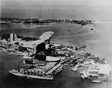A O2U floatplane flies over the Cavite Navy Yard, in 1930, below seaplane tender USS Jason and Sangley Point