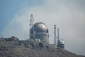 An observatory on a mountain, against a blue sky and a white cloud.
