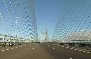 A three-lane motorway goes into the distance, flanked by blueish cables which hold up the Prince of Wales Bridge